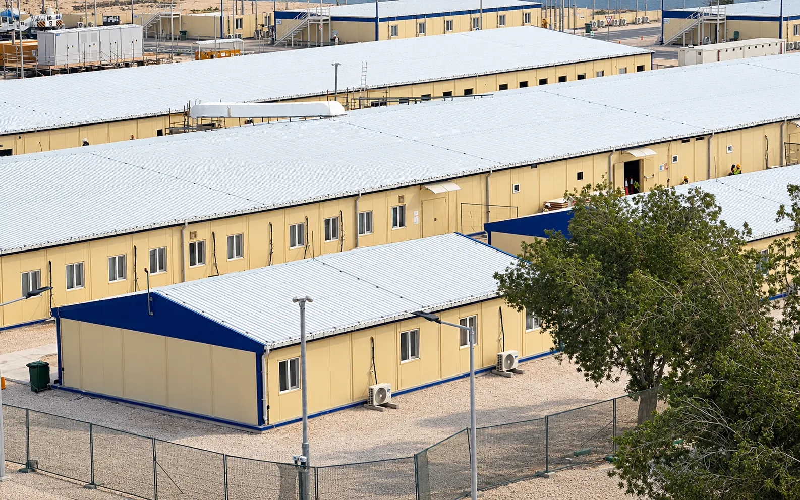 Aerial view of rows of single-storey yellow accommodation buildings with blue trim at a project camp in Qatar