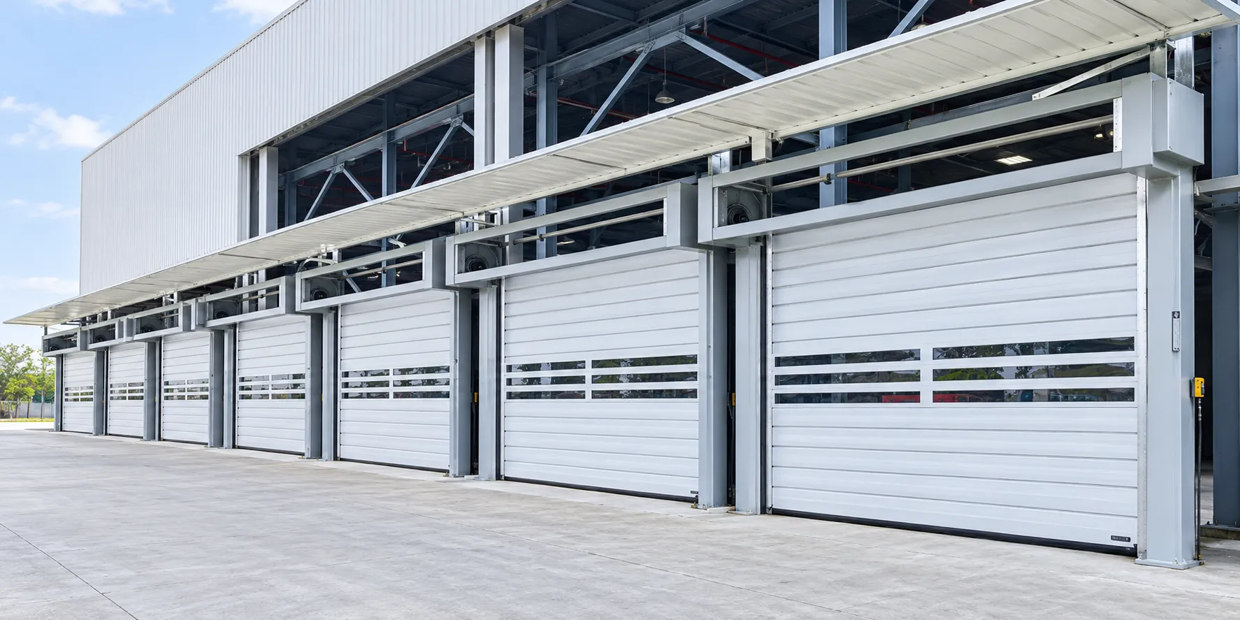 Row of white high speed spiral doors with vision panels under a canopy along an industrial building (rendering)