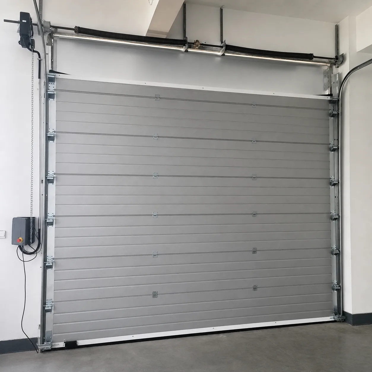 Silver-gray sectional door with twin torsion springs, side-mounted operator with chain hoist and control box