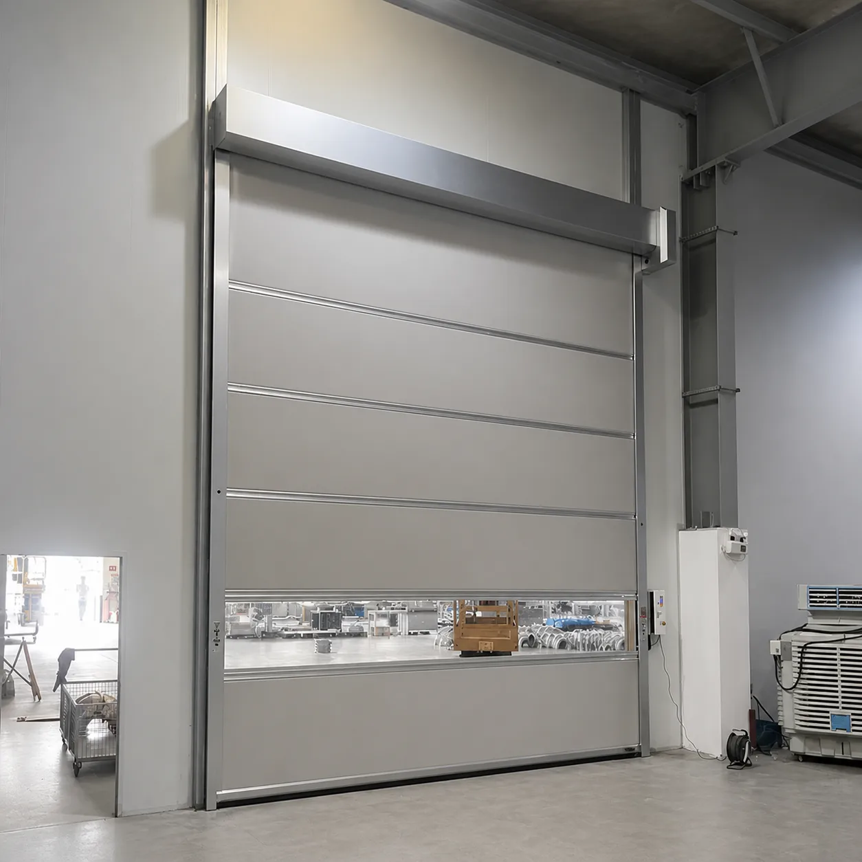 The same gray PVC high speed door seen at an angle, with the workshop visible through the vision strip