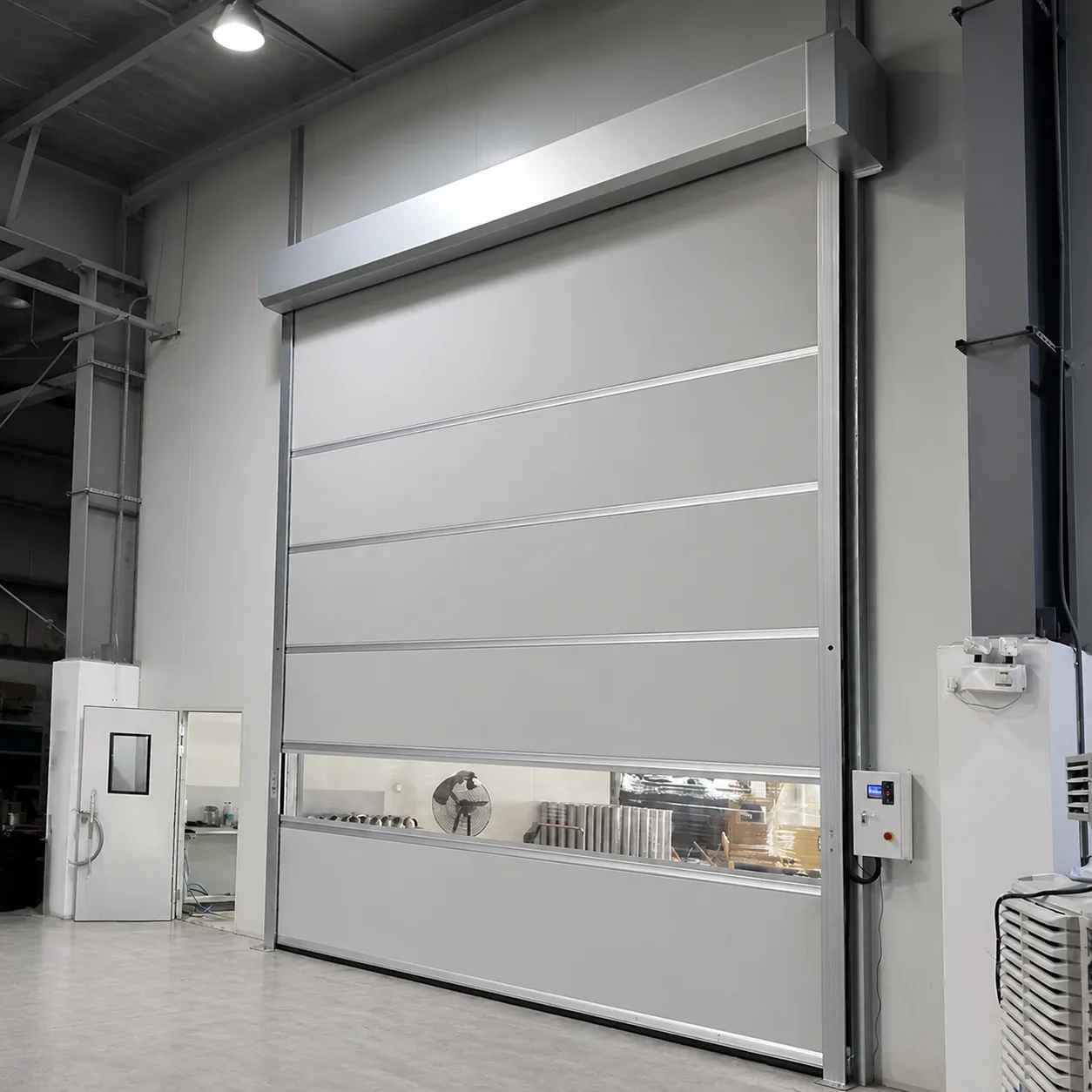 Gray PVC high speed door with a horizontal vision strip, motor cover and control box, installed in a workshop