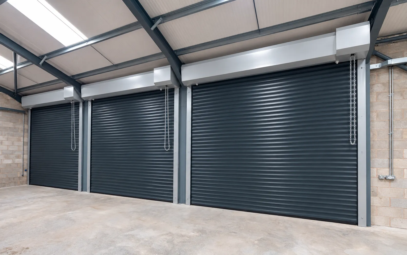 Dark grey prepainted steel roller shutters in an industrial workshop (rendering)
